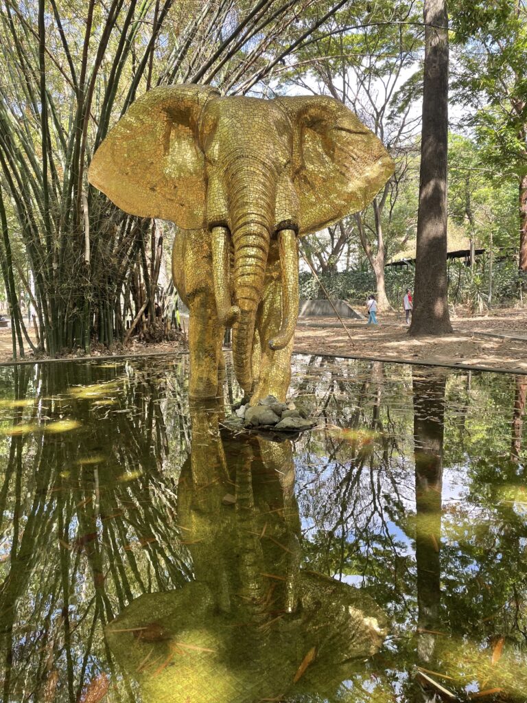 Escultura de elefante en tamaño real, de color dorado brillante, parado sobre pozo de agua en el Parque Los Caobos.